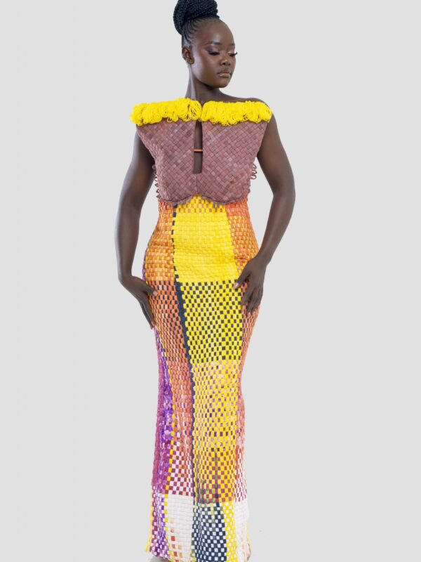 Plus qu’un vêtement, cette robe est une œuvre d’art, un dialogue entre force et couleur, entre tradition et modernité. Conçue pour la femme Kroskel qui avance avec assurance, elle incarne la puissance de celles qui tissent ensemble un avenir lumineux. Le buste, minutieusement travaillé, est inspiré des cases africaines et de leurs toits de paille. Les nœuds délicatement tissés viennent se poser comme des symboles de protection et d’ancrage, tandis que la couleur jaune éclatante illumine l’ensemble, porteuse d’espoir et de renouveau. Sa coupe majestueuse met en valeur la silhouette avec une jupe montante qui épouse la taille et vient se fixer au buste grâce à de sublimes petits boutons, créant une transition harmonieuse entre les textures et les volumes. Son dos nu et sa longue fente dans le dos apportent une touche de sensualité et de liberté, offrant une aisance parfaite à chaque mouvement. Réalisée en plus de 100 heures de travail, cette robe est un hommage au savoir-faire artisanal d’exception. Elle est destinée à celles qui osent, qui inspirent et qui laissent une empreinte indélébile sur leur passage.